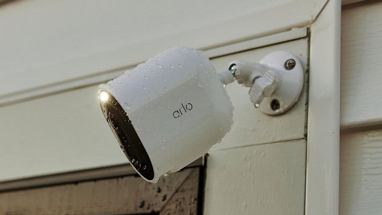 an arlo spotlight camera sits on the outside of a home, near the garage and is covered in rain drops
