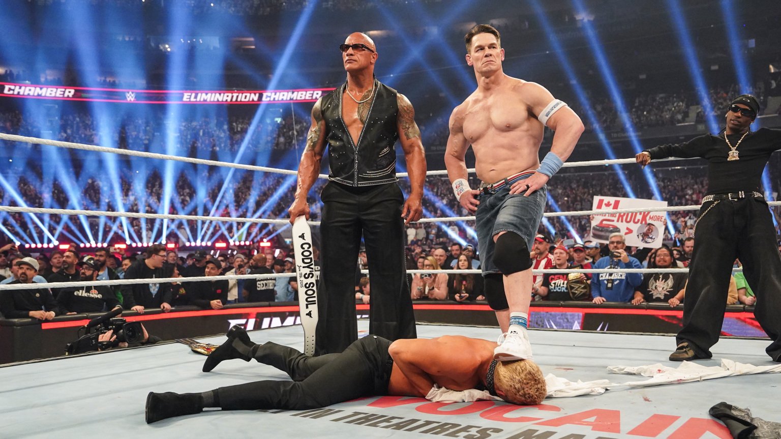 The Rock and John Cena stand over Cody Rhodes at WWE Elimination Chamber
