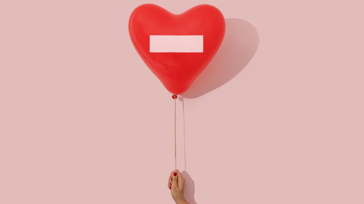 Woman's hand holding a heart shaped red ballon with a prohibited sign