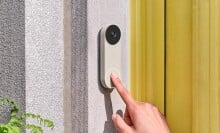a person's right index finger approaches touching the google nest video doorbell that's affixed next to a home's front door