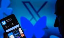 Bluesky's butterfly logo covers an X while a man looks at the Bluesky app on his phone