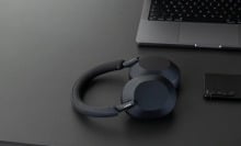 a pair of sony headphones sits on a black desk with a laptop and cell phone