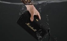 a person's left hand submerges the marshall middleton speaker into water
