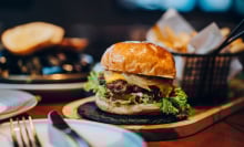 a burger on a wooden board with a little basket of fries. 