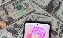 An Instagram logo seen displayed on a smartphone with United States Dollar notes and coins in the background.