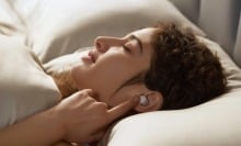 a person in bed touches an index finger to an anker sleep a20 earbud that's in her ear
