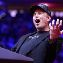 Elon Musk screaming at a Trump rally wearing a 'dark MAGA' hat