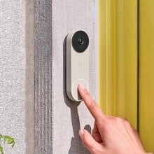 a person's right index finger approaches touching the google nest video doorbell that's affixed next to a home's front door