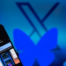 Bluesky's butterfly logo covers an X while a man looks at the Bluesky app on his phone