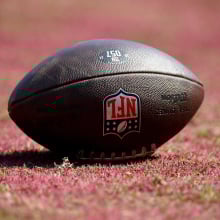  A close up view of a Wilson official NFL "The Duke" brown leather football with NFL shield logo on painted red / burgundy natural grass in the end zone during the New York Giants versus Washington Commanders National Football League game