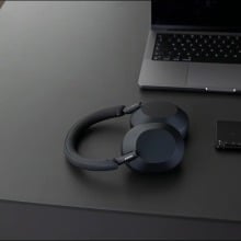 a pair of sony headphones sits on a black desk with a laptop and cell phone