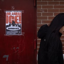A woman walks in front of a poster that reads, "No abran a ICE!"