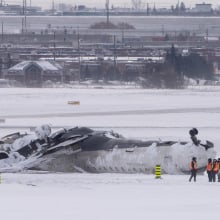 Airport workers survey the site of a Delta Air Lines plane crash that injured at least 18 passengers at Toronto Pearson International Airport on February 18, 2025 in Toronto, Canada. The jet, coming in from Minneapolis, attempted to land amid strong winds and snow, leading to it crashing and landing upside down on the tarmac the day before.
