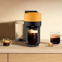 a mango yellow nespresso vertuo pop+ coffee maker sits on a countertop with several coffee drinks