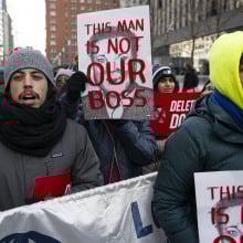 A group of federal workers protesting on the streets of New York. They hold signs with Elon Musk's face that read "This man is not our boss."