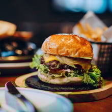 a burger on a wooden board with a little basket of fries. 