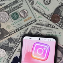 An Instagram logo seen displayed on a smartphone with United States Dollar notes and coins in the background.