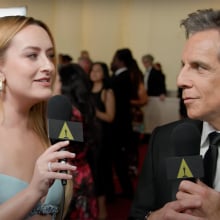 A woman stands on the red carpet interviewing a man in a suit.