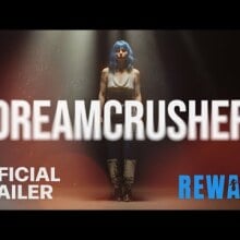 A woman in a blue wig behind the text "Dreamcrusher."
