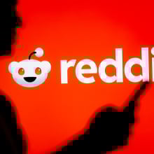 person looking at a smartphone with a Reddit logo displayed in the background