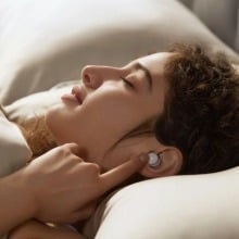 a person in bed touches an index finger to an anker sleep a20 earbud that's in her ear