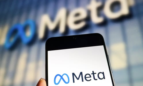 A phone displaying the Meta logo held up in front of a Meta office building.