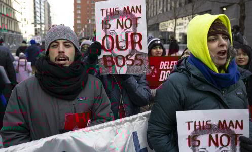 A group of federal workers protesting on the streets of New York. They hold signs with Elon Musk's face that read "This man is not our boss."