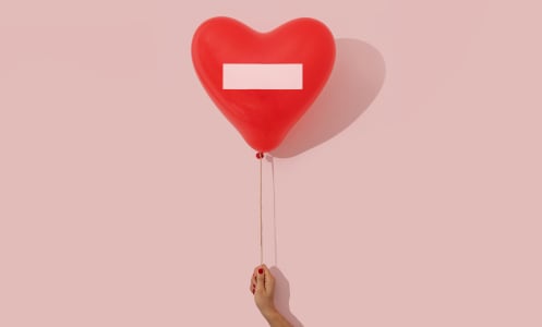 Woman's hand holding a heart shaped red ballon with a prohibited sign