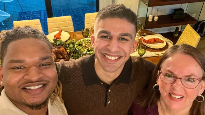 Jamal Hinton, Wanda Dench, and an unidentified male guest standing in front of a dining table set with a Thanksgiving dinner.