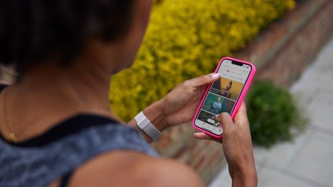 a person walking looks at a smartphone that shows the Peloton app