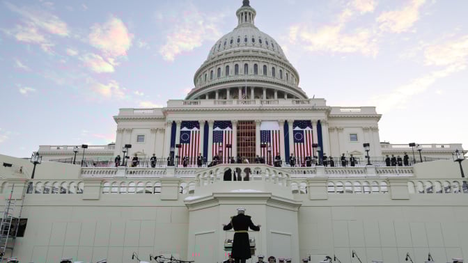 The United States Marine Band rehearsing their performance in front of the Capitol building, as large American flags drape across the facade.