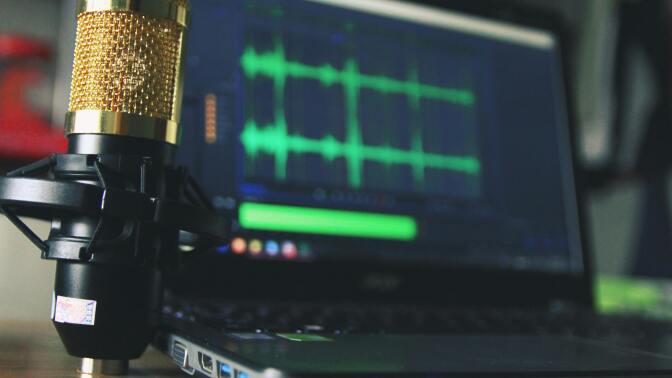 a condenser microphone next to a laptop with audio editing software