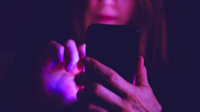 A woman using smartphone at night under colorful LED lights
