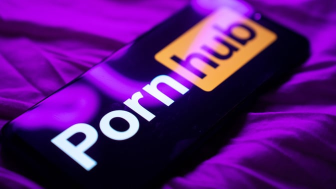 phone with the logo of Pornhub on its screen in purple sheets below purple lighting