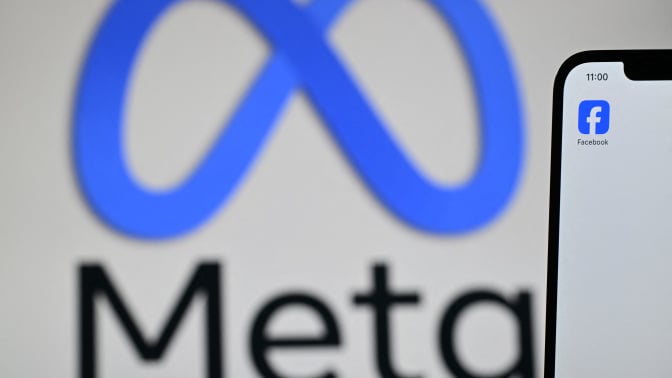  Meta logo is displayed on a laptop screen next to the Facebook app displayed on a phone screen, in a residential property in Guildford, south of London.