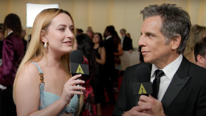 A woman stands on the red carpet interviewing a man in a suit.