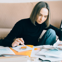 a woman in a black turtleneck and jeans doing her taxes at a coffee table while sitting in front of a brown couch