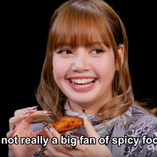 Lisa holding a chicken wing on "Hot Ones."